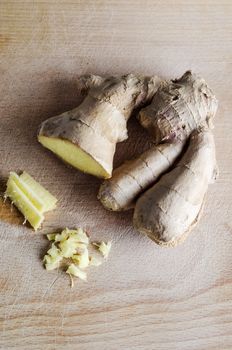 Overhead shot of whole, sliced and roughly chopped ginger root on an old, used  wooden chopping board with many knife cuts on it's surface.