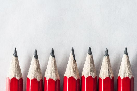 A row of roughly sharpened, grubby red pencils on textured art paper, bordering the bottom of the frame.  Lit and processed to give an old fashioned, vintage appearance.