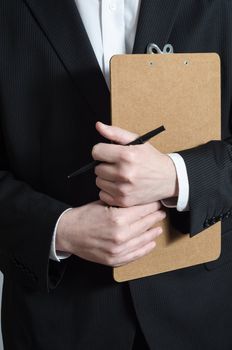 Close up crop shot of a male (torso) in a dark suit and white shirt, holding a clipboard and pen, waiting to collect research data or to confirm a booking or check his list.