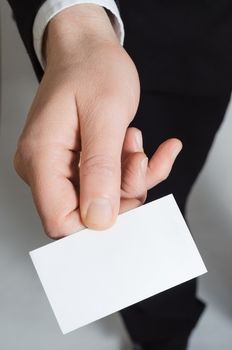 Close up of the hand of a man in a suit, reaching forward holding a blank business card facing upwards towards the viewer.