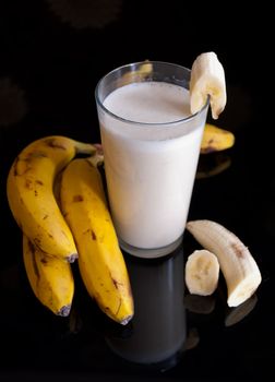 fresh banana smoothie and fruits on black background