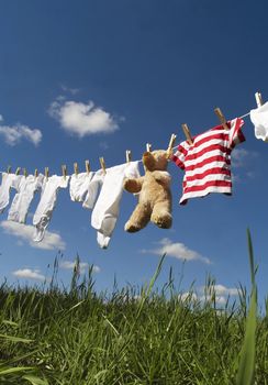 Baby Clothing and a teddybear on a clothesline towards blue sky