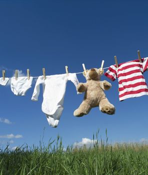 Baby Clothing and a teddybear on a clothesline towards blue sky