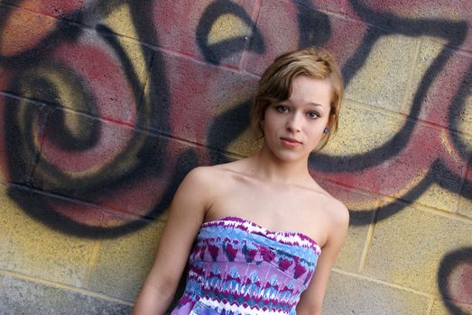 A young attractive woman poses next to some city graffiti.
