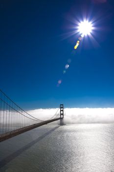 Photo of the golden gate bridge, san francisco, with fog covering one end, a blue sky and the sun in one corner.