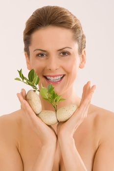 Laughing woman with open eyes and relax with pebbles and a herb in your hand.