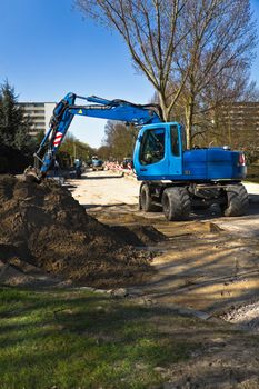 Draglines at work to renew the pavement of a road in the city. Blue excavators and bright blue sky in early spring. Vertical image.