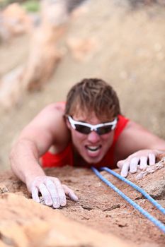 Man climbing. Strong male climber in difficult challenge during rope rock climbing. Focus on hand in foreground.