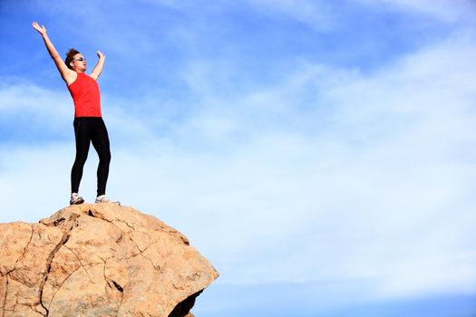 Success - winner reaching summit. Athlete in fitness sport clothes and running shoes reaching the goal cheering with arms raised. Man fitness model happy with lots of copyspace on blue sky.