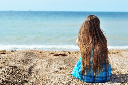 young longhaired woman sitting alone at the beach 