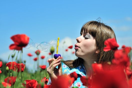 young woman blowing soap bubbles on the poppy field