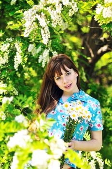 longhaired girl holding bunch of daisies and standing near acacia 