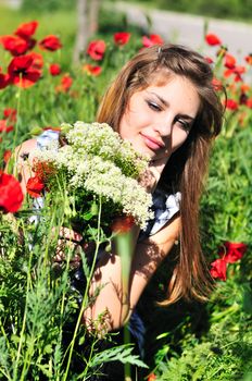 girl with bunch  of wild flowers sitting in the poppy field