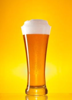 Full glass of beer with froth over yellow background 