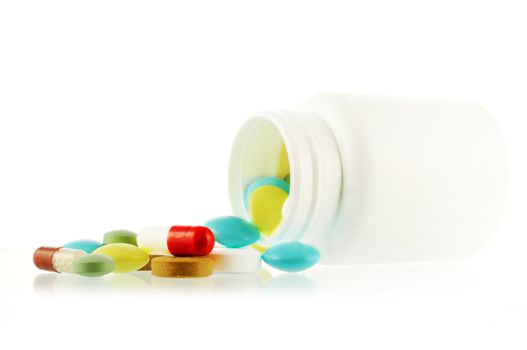 Bottle with falling out many-coloured pills on white background