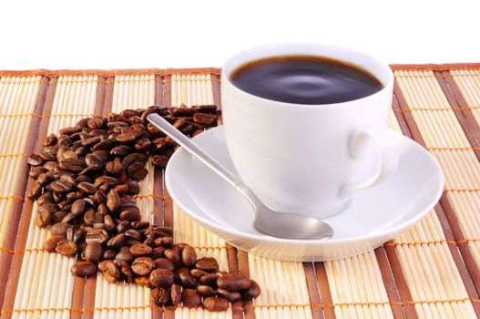 White cup with coffee on bamboo mat and coffee beans