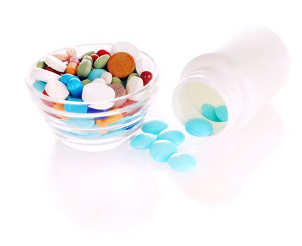 White bottle with blue tablets and transparent saucer with many-colored pills