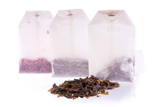 Three teabags with dry tea and heap of black tea. Focus on a first teabag.