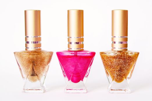 Three bottles with nail varnish: one pink and two golden colours