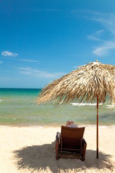 Unrecognizable person reading book in canvas chair on beautiful tropical beach 