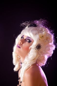 Portrait of young woman in white colonial wig, studio shot on purple background 