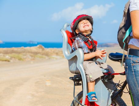 Cute boy sitting by bicycle seat in crash helmet. Vertical view