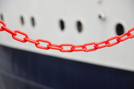Red chain in front of white and blue hull of a ship