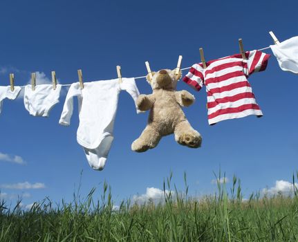 Baby Clothing and a teddybear on a clothesline towards blue sky