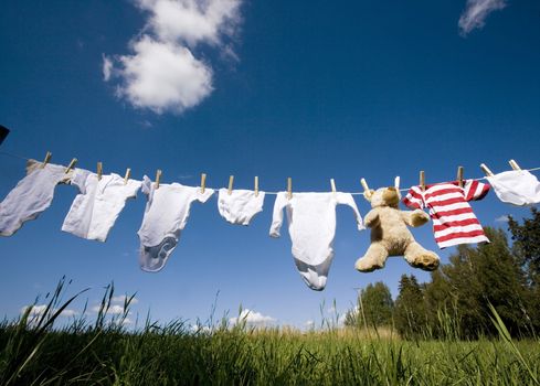 Baby Clothing and a teddybear on a clothesline towards blue sky