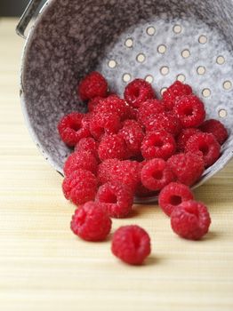 Photo of fresh raspberries spilling out of a metal colander.
