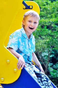 funny boy on a blue-yellow playground slide 