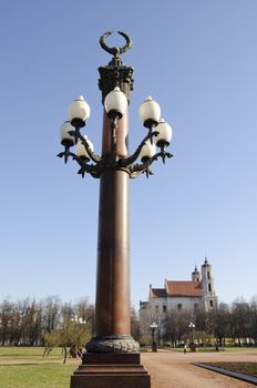 park decorative antique lamp in center of city lukiskes square. church building in distance.