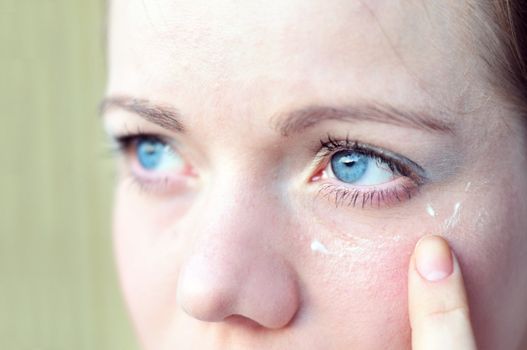 close-up of woman's eyes, she applying a cream in soft selective focus