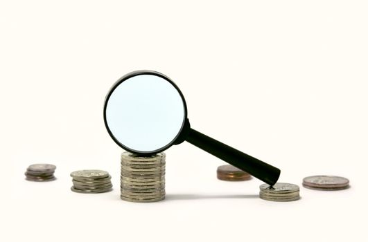 Magnifier on a pile of coins isolated on white