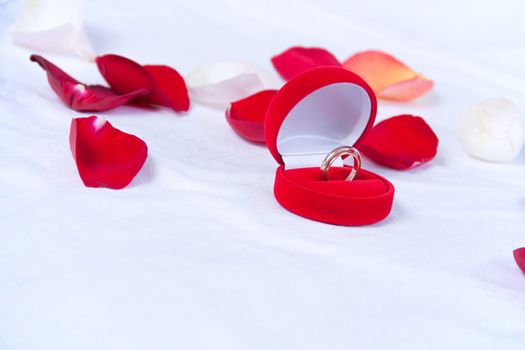 Wedding rings in the red box lie on the bed with rose petals