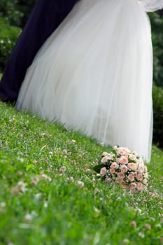 bridal bouquet lies on the grass next to the bride and groom are kissing