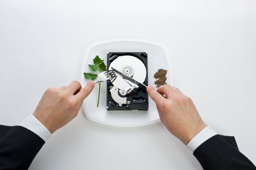 hard drive is on the dining plate with seasoning and herbs. man's hands cut drive a knife and fork