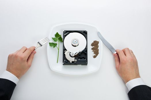 hard drive is on the dining plate with seasoning and herbs. Men's hands hold a knife and fork