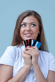 young woman holds credit cards and pensively smiles. Business style