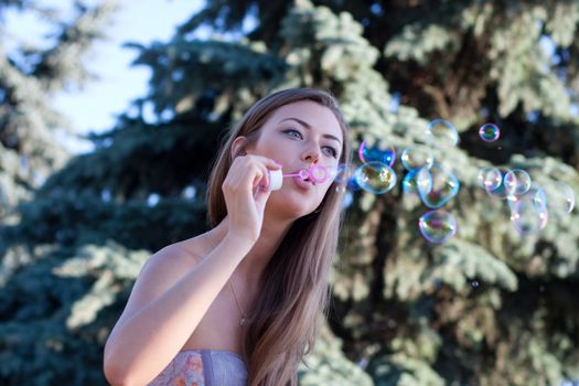 young woman makes soap bubbles sitting on a bench in park