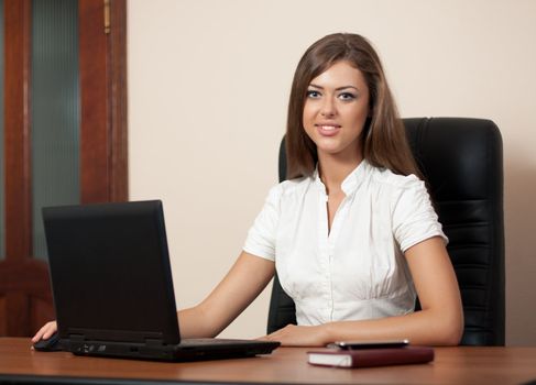 young woman sits at a table at office with the laptop and looks in the chamber. Business style