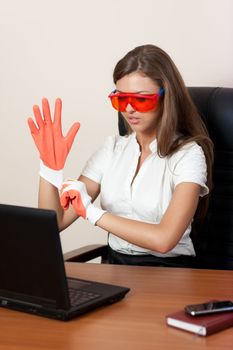 young woman sits at a table at office in orange glasses dresses gloves and looks in the laptop. Business style.