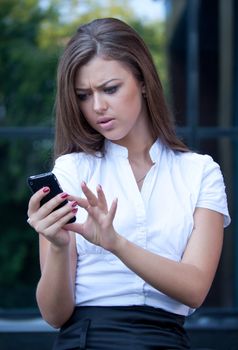young woman looks in a cellular telephone and is angry having seen something on the screen. Business style