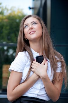 young woman with phone in hands smiles looks upwards. Business style.