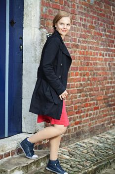 Pretty smiling young blond woman walking out of the door of an old brick house