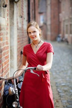 Young blond woman in red dress standing on a street with old bicycle