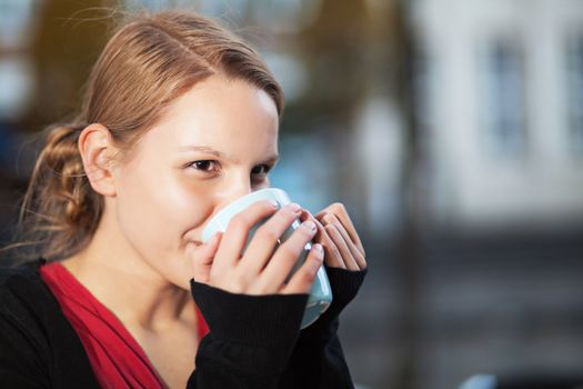 Pretty young woman drinking hot drink from a ceramic cup outdoors