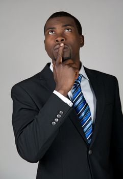 African American businessman looking up and thinking, holding a finger on his lips.