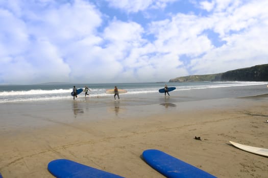 sandy golden beach with surfboards lying on the sand and children running into the sea to surf in ballybunion county Kerry Ireland
