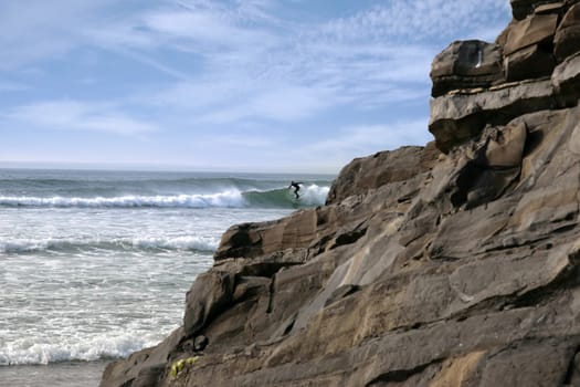 beautiful clean atlantic ocean with lone surfer catching the waves with cliffs and rocks in foreground on Irelands coast